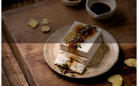 Silk tofu japanese soy cheese whole piece with chili ginger, chive and soy sauce topping on ceramic plate over wooden table.